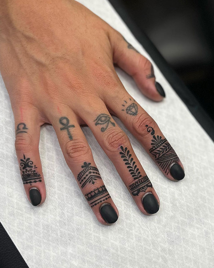 Hand with black finger tattoos featuring intricate designs on each finger.