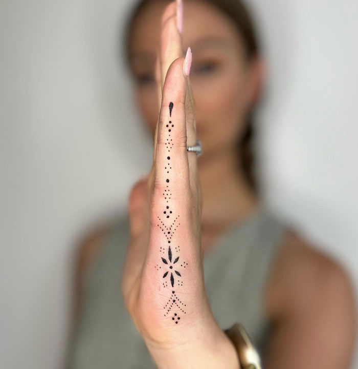 Delicate black dotwork finger tattoo design on the side of a woman's hand in focus.