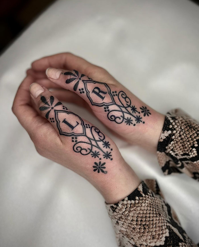 Decorative finger tattoos with intricate black designs featuring letters "L" and "R" on hands.