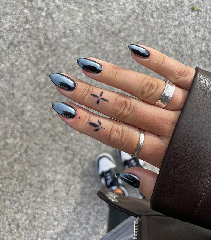 Close-up of modern finger tattoos and silver rings on manicured hand with metallic nail polish.