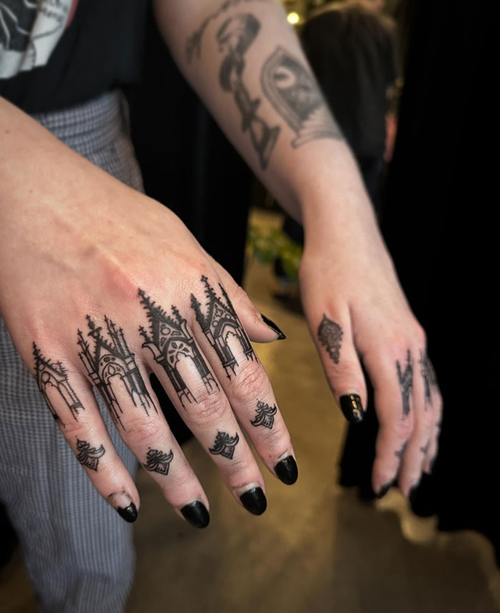 Detailed finger tattoos with gothic designs and black nail polish.