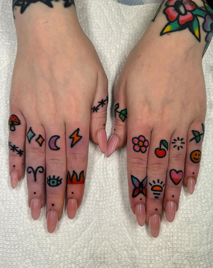 Colorful finger tattoos featuring various designs like flowers, cherries, and symbols on both hands.