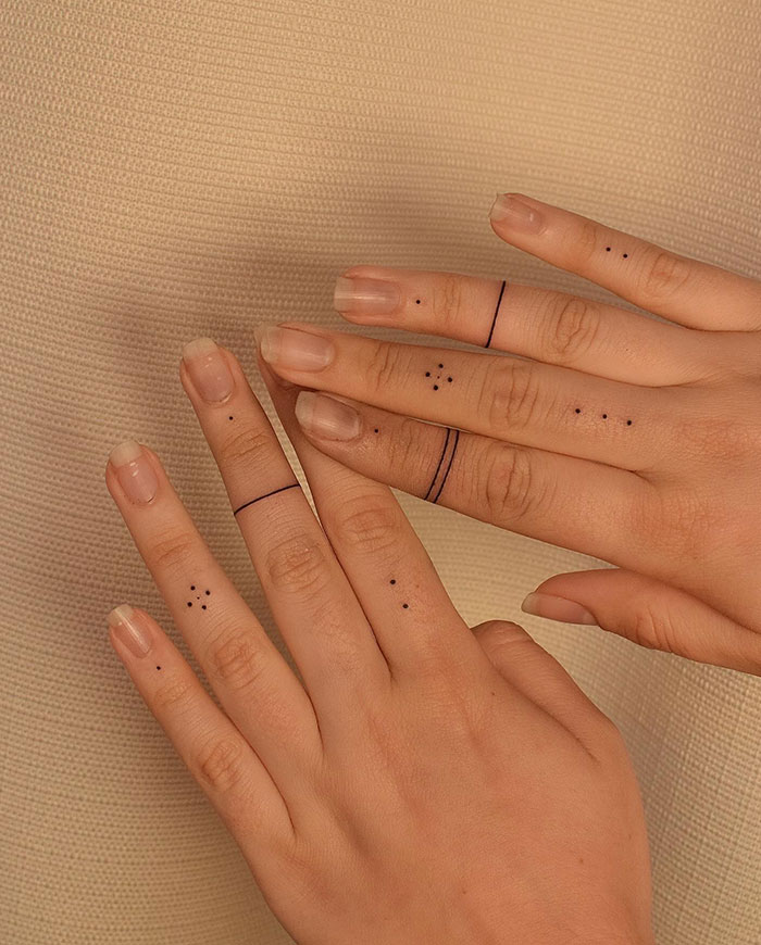 Minimalist finger tattoos featuring dots and lines on hands.