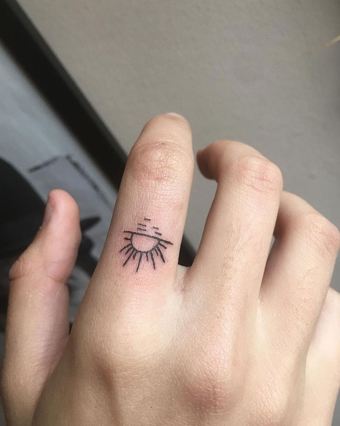 Minimalist finger tattoo featuring a sun design on a person's finger.