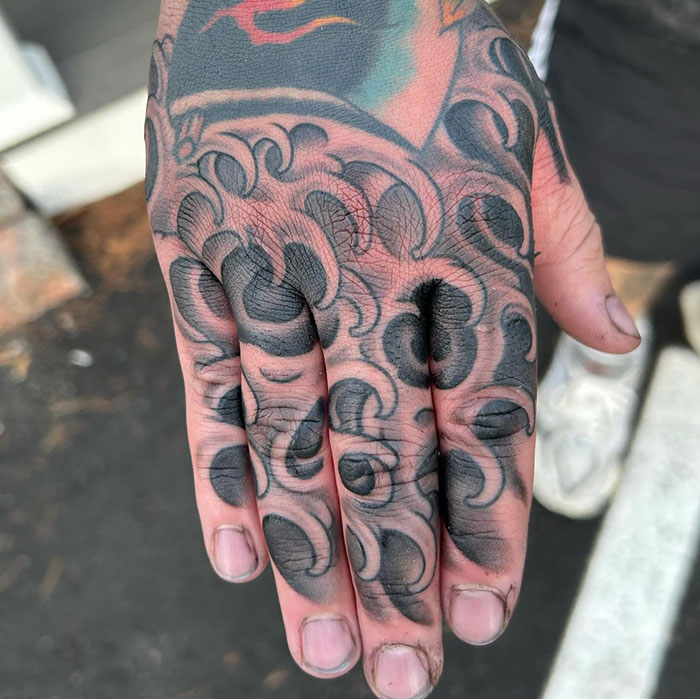 Intricate finger tattoos with swirling black designs covering fingers and hand.