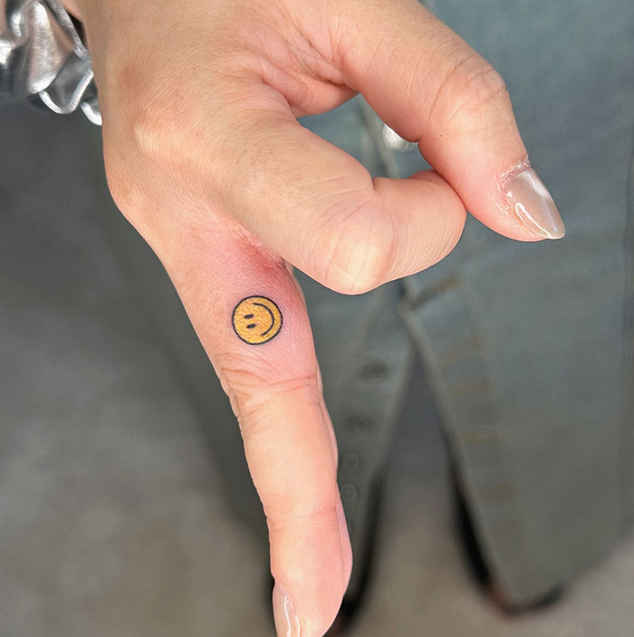 Close-up of a hand with a smiley face finger tattoo, showcasing unique finger tattoo designs.