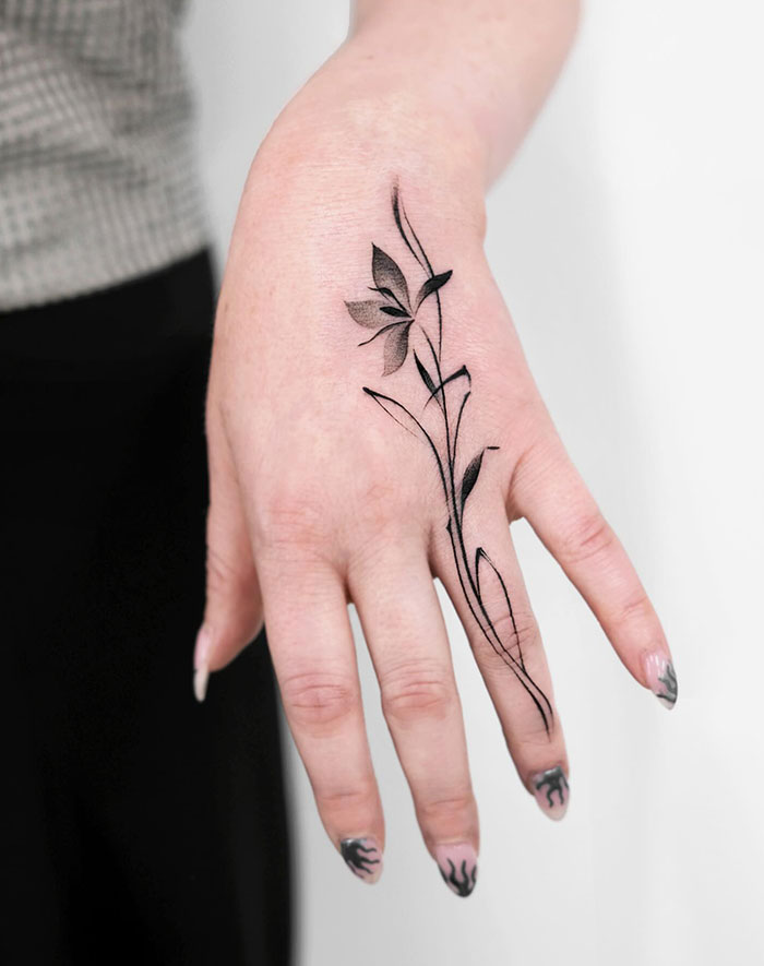 Floral finger tattoo on a hand, showcasing elegant and intricate linework design.