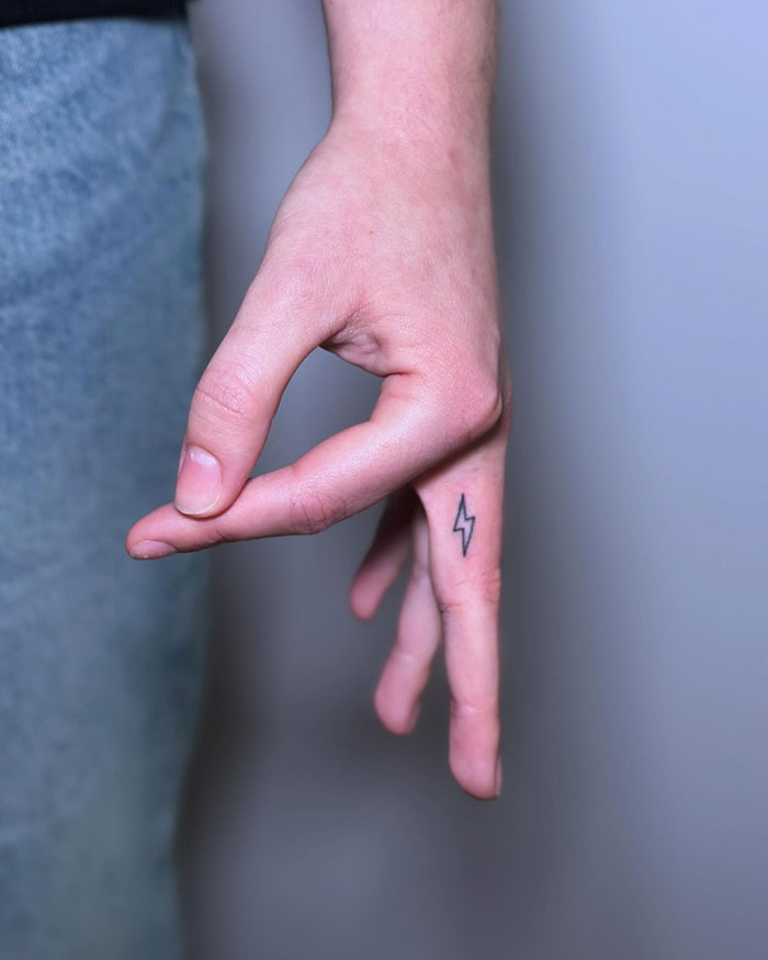 Minimalist finger tattoo featuring a small lightning bolt design on the side of a pinky finger.