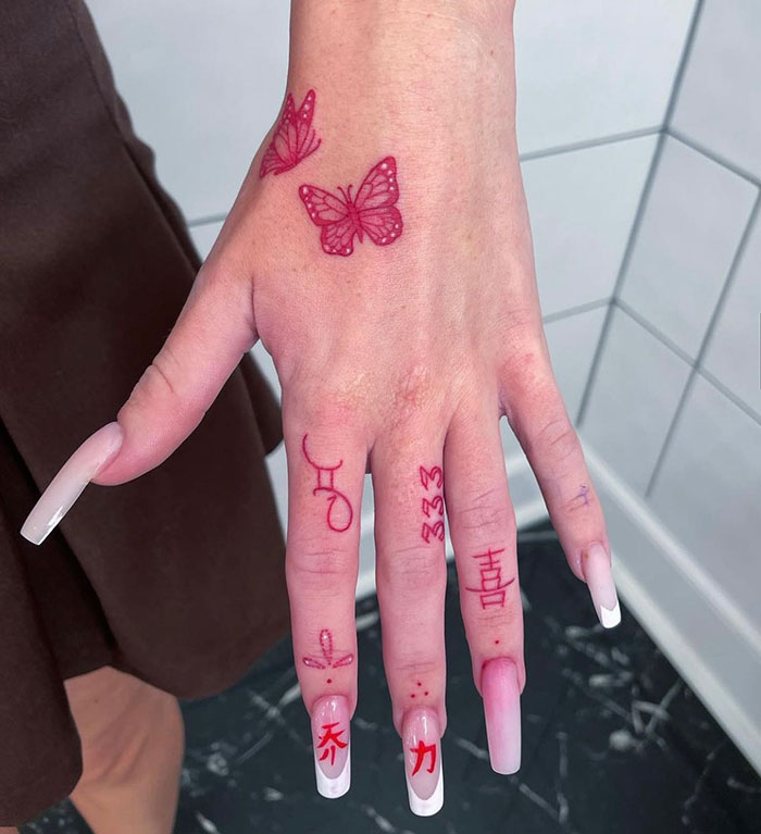 Red finger tattoos including symbols and butterflies on a woman's hand.