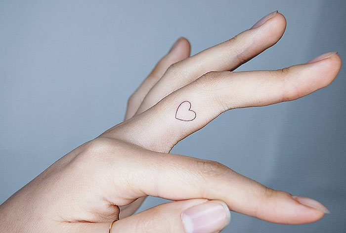 Minimalist heart finger tattoo design on the side of a finger.