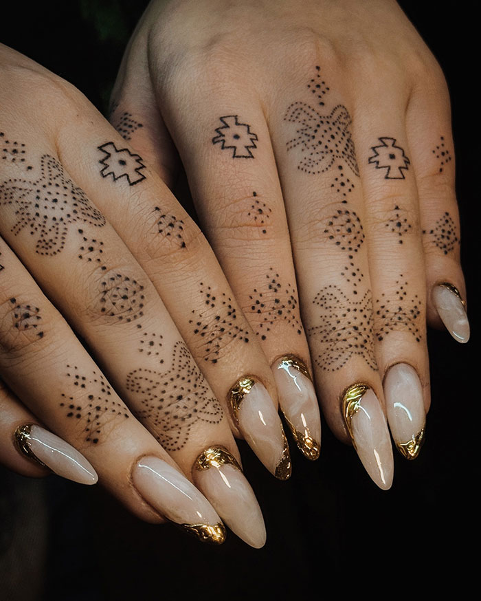 Intricate finger tattoos with geometric patterns and glossy, gold-tipped nails.