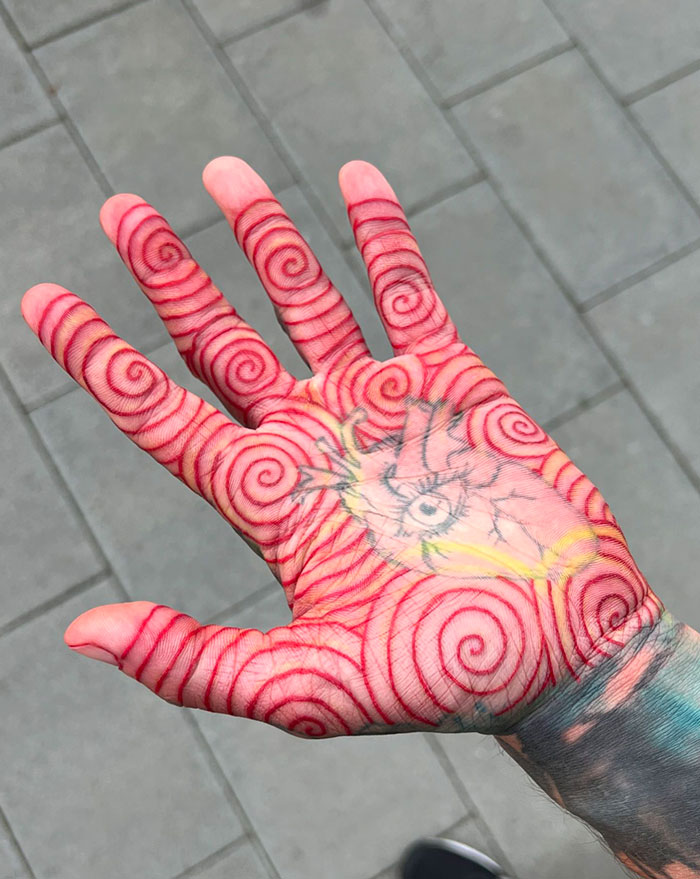 Hand with intricate finger tattoos featuring red spiral patterns and an eye design in the palm.