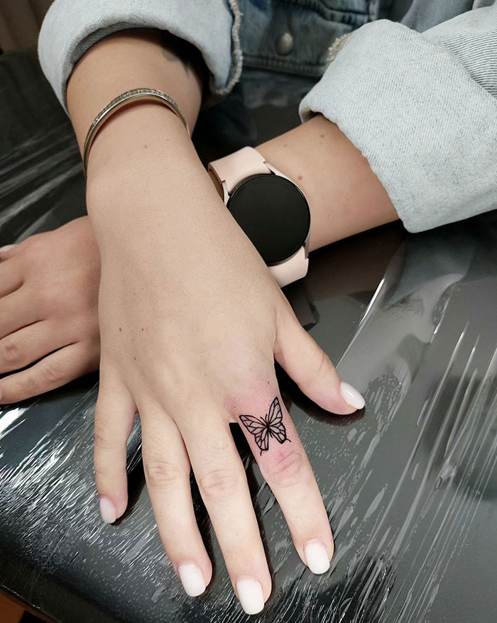 Butterfly finger tattoo on a person's hand with a watch and bracelet, showcasing a minimalist design.