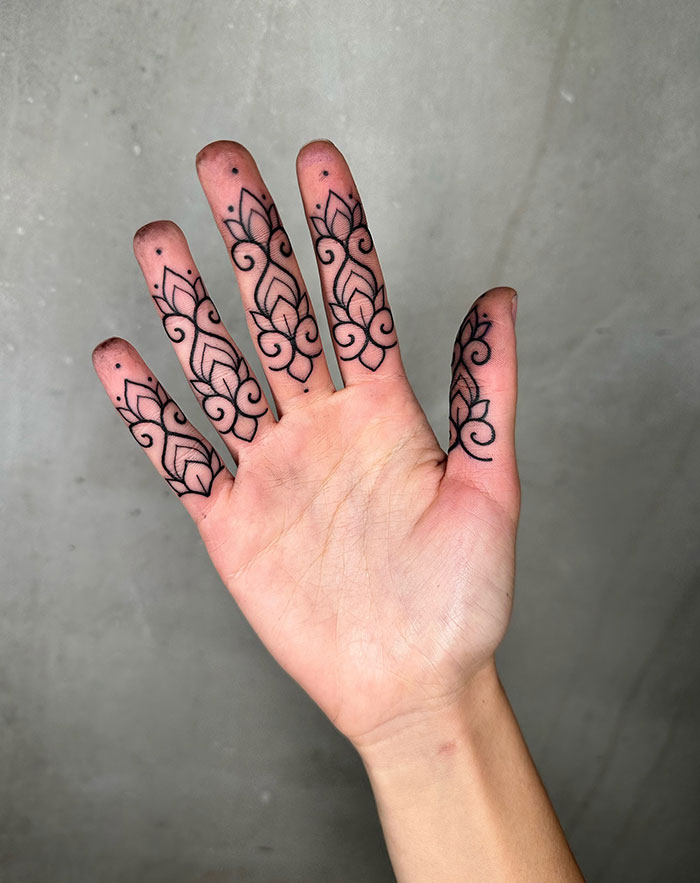 Ornate finger tattoos with black ink floral patterns on fingertips and knuckles.