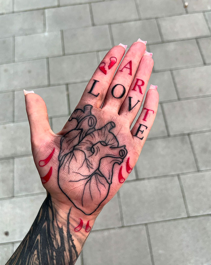 Hand with intricate finger tattoos displaying "ART" and "LOVE" over a heart design.