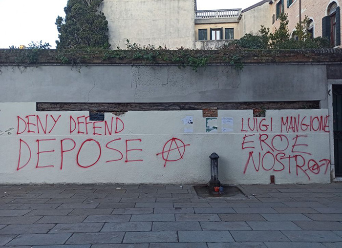 Graffiti on a wall referencing Luigi Mangione, with phrases in red paint, against an urban background.