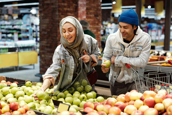 Couple shopping for apples at a grocery store, woman looks excited, both holding fruit.