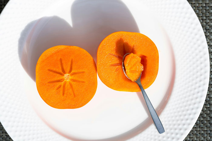 Two halves of an orange fruit, with one half scooped by a spoon, on a white plate.