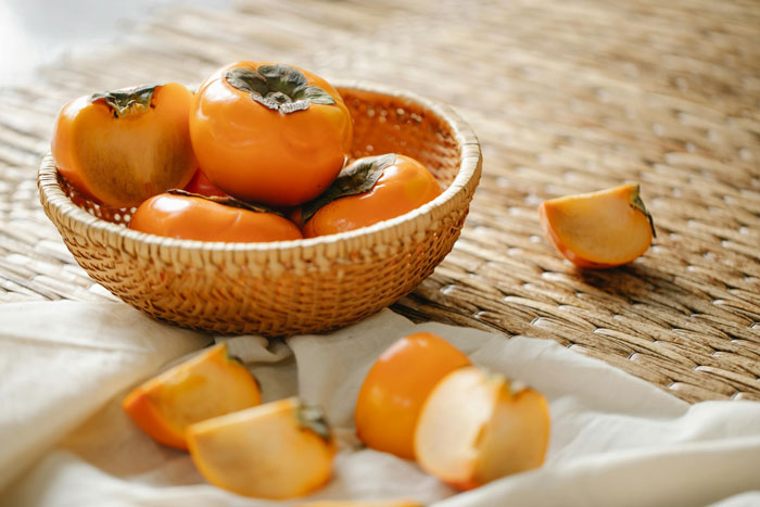 Basket of fresh persimmons on a woven mat with sliced pieces nearby, highlighting fruit obsession.