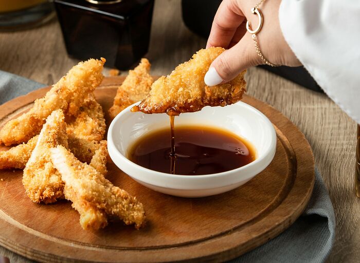 Dipping breaded chicken into sauce, possibly depicting a traveler's cringeworthy food experience.