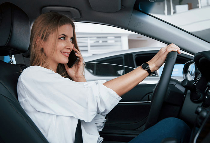 Woman on phone driving, illustrating friend taking forever to repay debt.