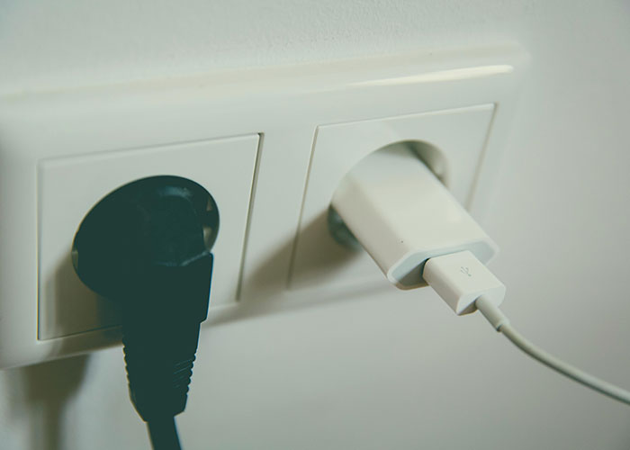 Close-up of two plugs in a wall socket, illustrating creative frugal hacks to save cash.