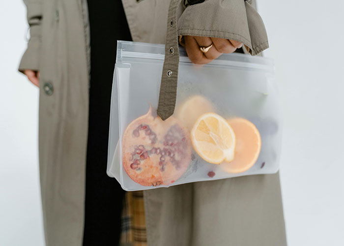 Person holding a reusable bag with citrus fruits, showcasing creative frugal hacks for saving cash.