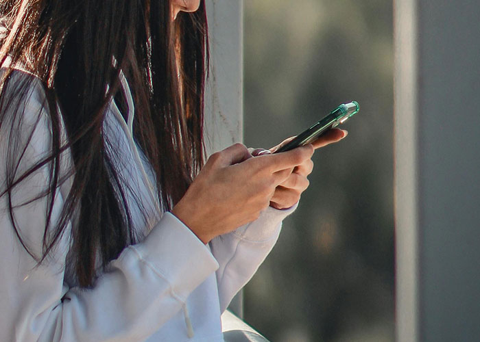 A woman in a white hoodie using her phone, possibly sharing creative frugal hacks to save cash.