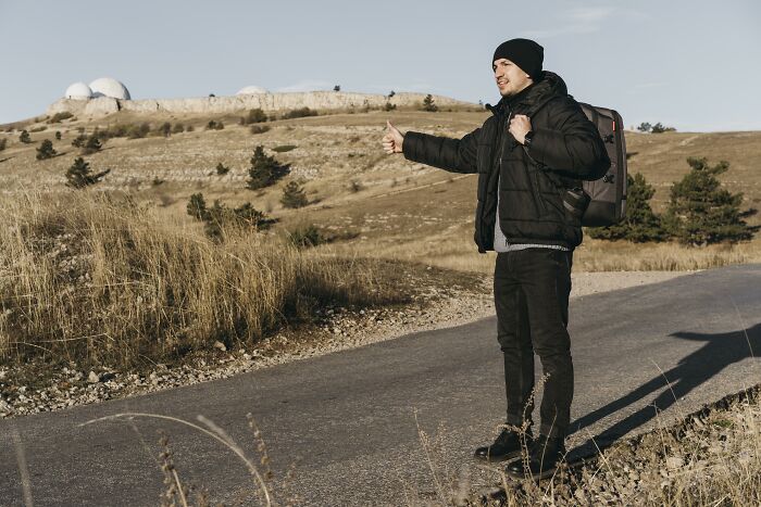 Man hitchhiking on a rural road with observatories in the background, illustrating an astonishing coincidence.