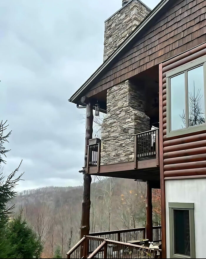 Oddly positioned chimney on a log cabin, showcasing a hilarious construction fail against a cloudy sky.