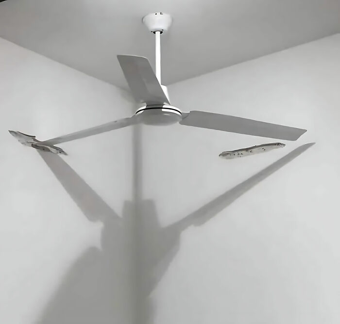 Ceiling fan installed partially inside the wall corner, showcasing a humorous construction fail.