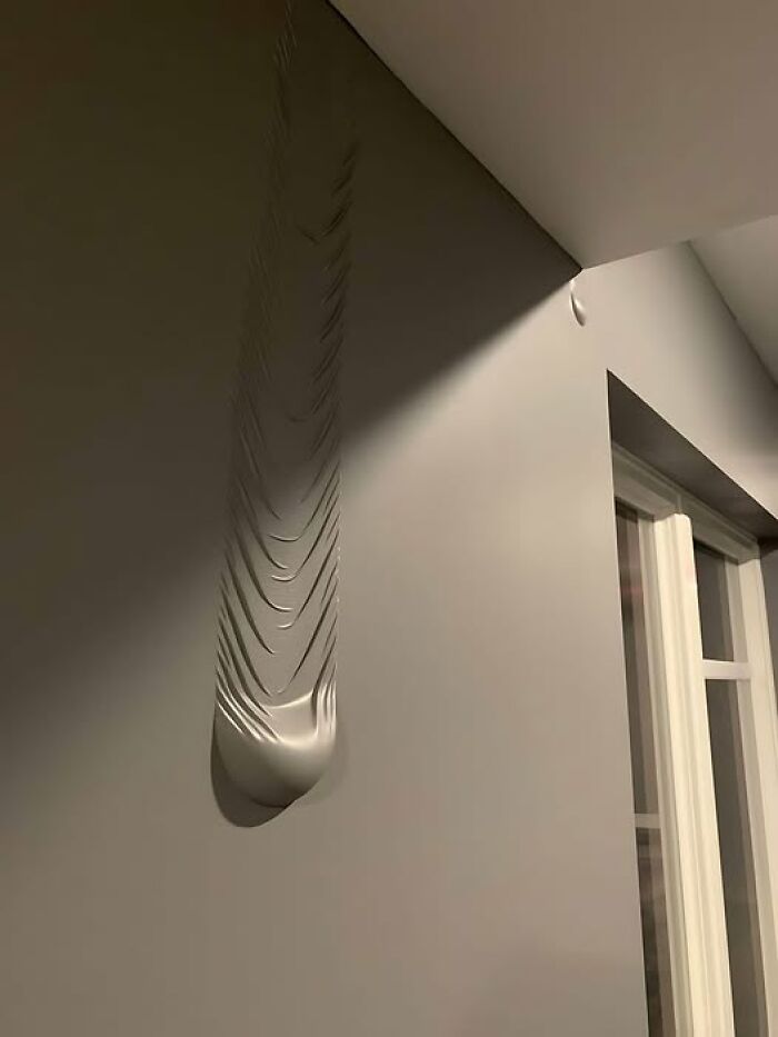 Wall with uneven plaster bulges creating a construction fail, casting shadows near a window.