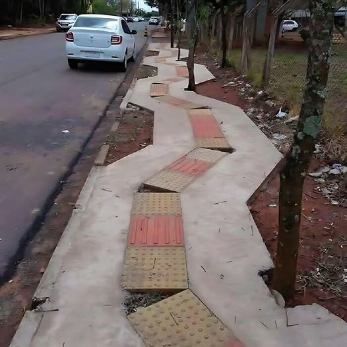 Zigzagging sidewalk with misplaced tiles showing a construction fail along a street with parked cars.