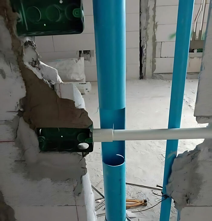 Construction fail with misaligned blue pipes and broken wall in a building under renovation.