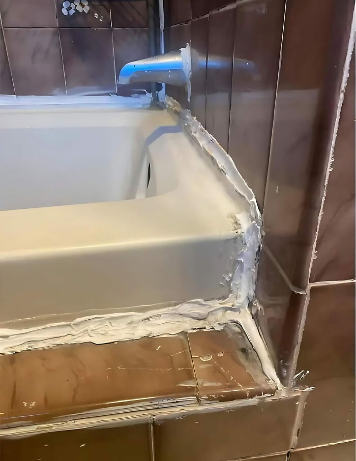 Bathroom construction fail with misaligned tiles and excessive sealant application around the bathtub.