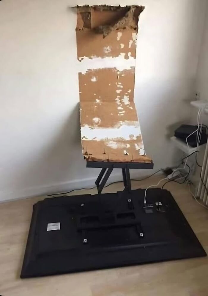 Broken TV stand leaning against a torn wall, showcasing a construction fail.