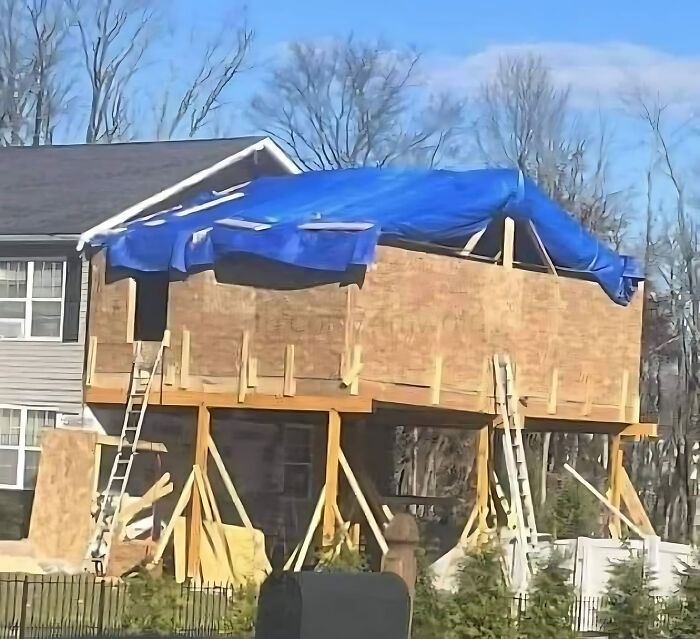 House under construction with uneven supports and a tarp roof, showcasing a construction fail.