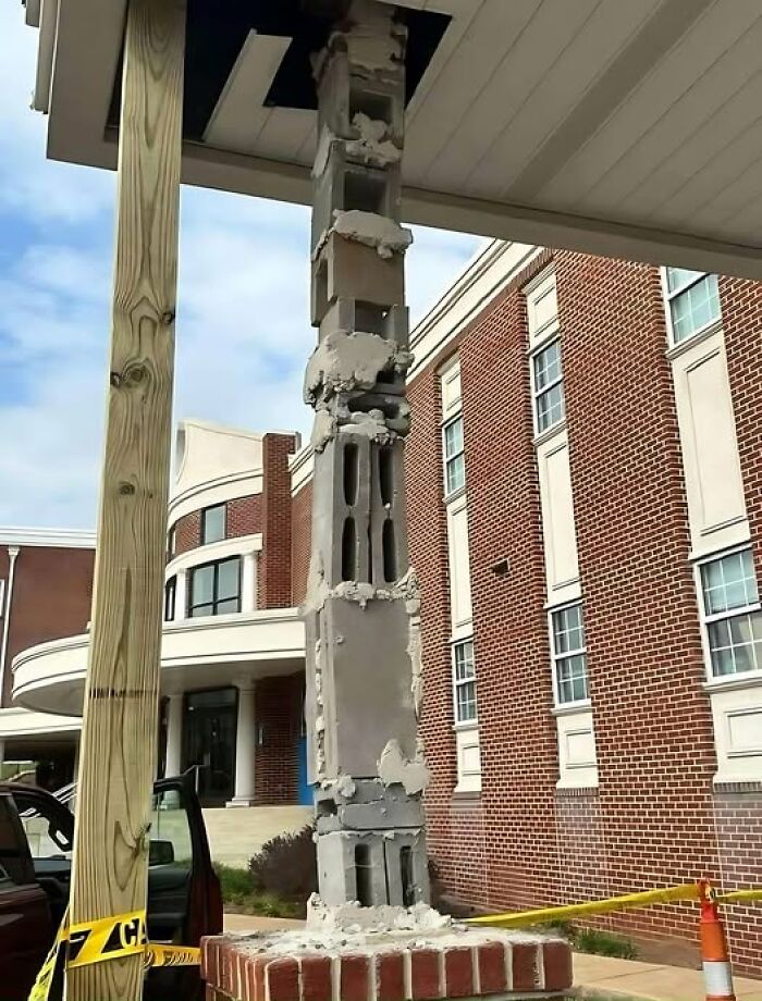 Damaged pillar with exposed cinder blocks in front of a brick building, showcasing a construction fail.