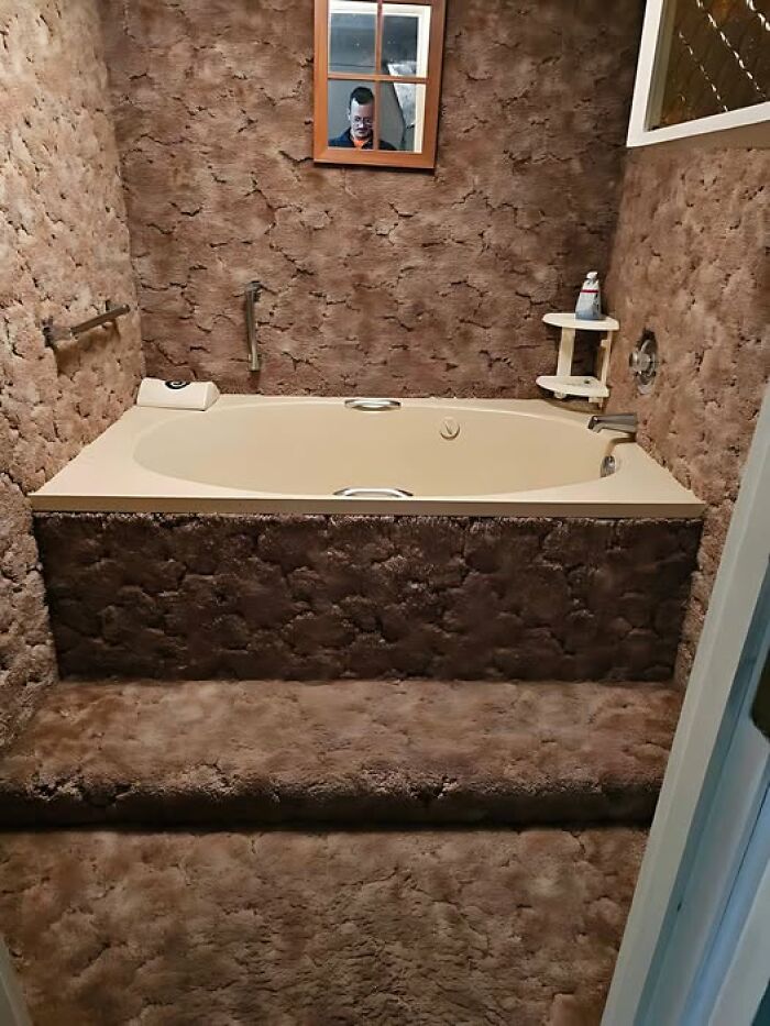 Bathtub covered in brown carpet with a mirror reflection; example of construction fails.