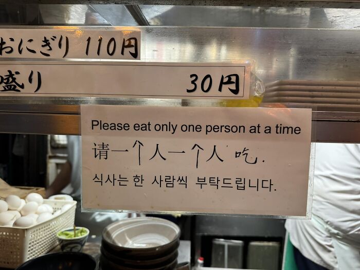 Sign with translation error in Japan: "Please eat only one person at a time," alongside dishes and menu prices.