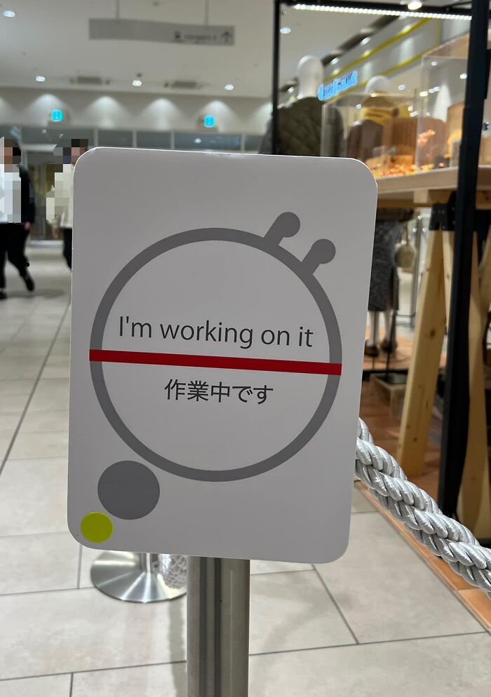 Sign in Japan with humorous translation error saying "I'm working on it" in a shopping area.