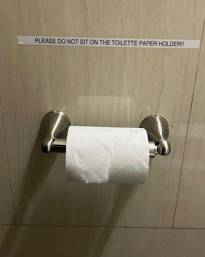 Toilet paper holder with humorous sign in New York bathroom.