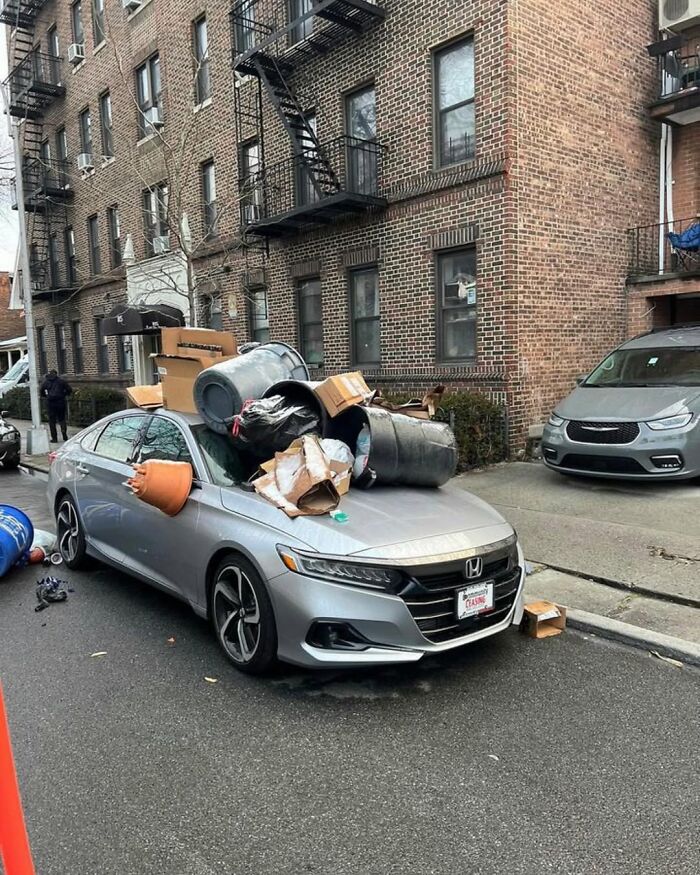 A car in New York covered in trash bags and boxes, parked on a city street.