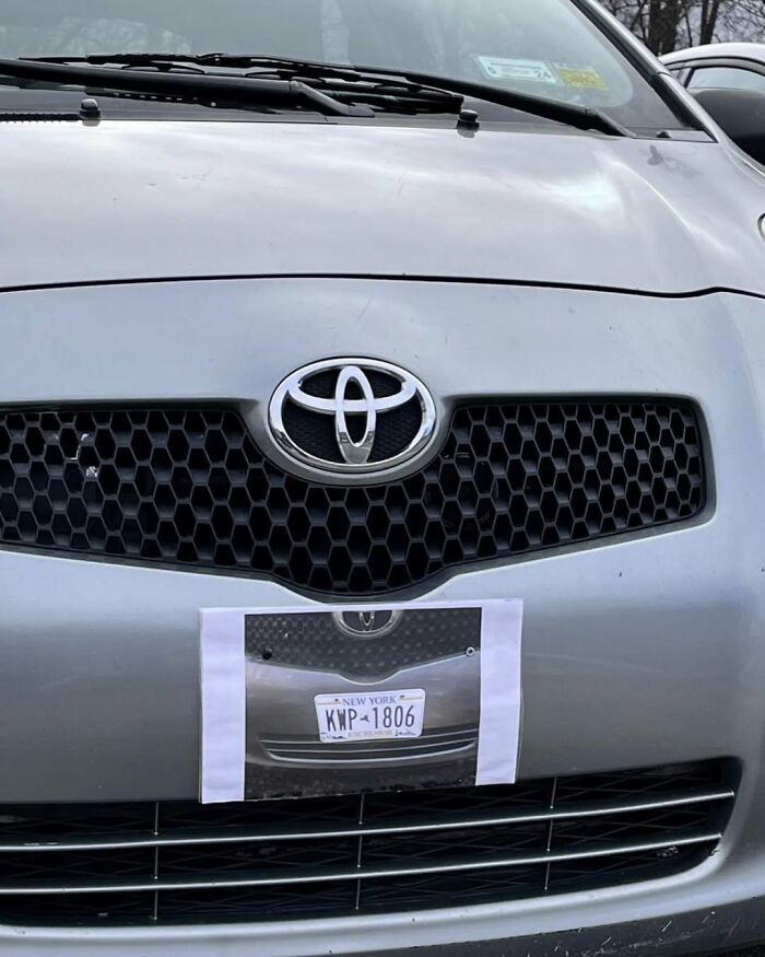 Car with a printed New York license plate taped on the front bumper, humorously imitating a real plate.