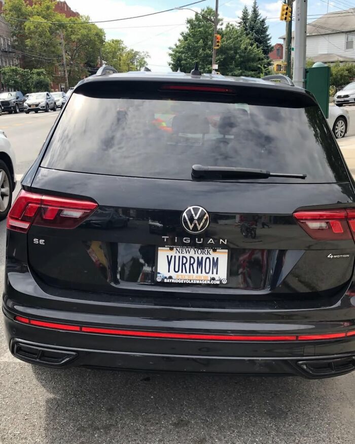 Black Volkswagen Tiguan with a humorous New York license plate reading "YURRMOM" parked on a street.