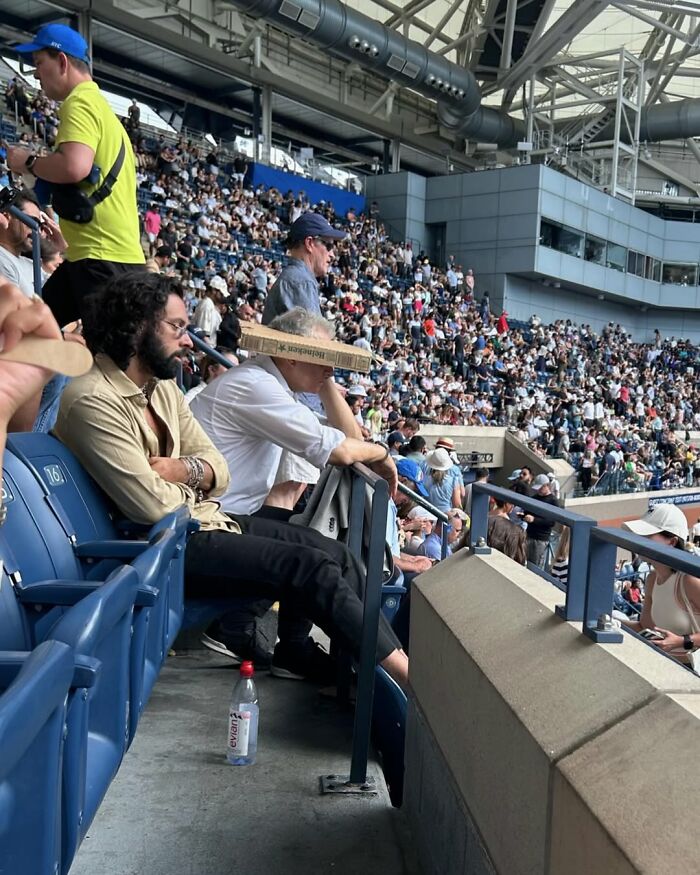 A man in a stadium uses a pizza box as a hat in New York, surrounded by a large crowd.