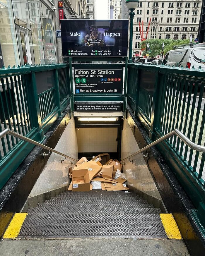 Boxes piled up at New York's Fulton St Station entrance, adding humor to the bustling city scene.