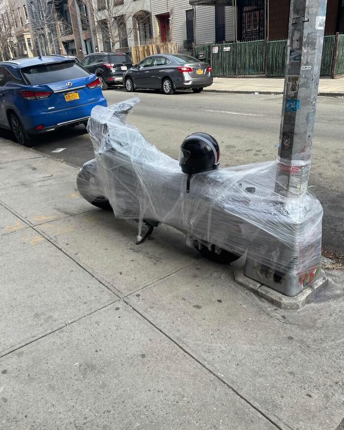 Motorbike wrapped in plastic by a pole on a New York street, reflecting the quirky cityscape.