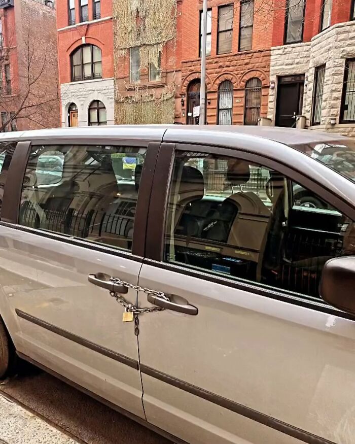 Van in New York with chain and padlock securing door handles, parked on a street with brownstone buildings.