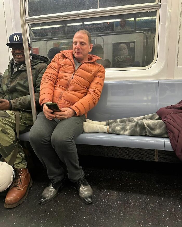 Funny scene on New York subway: man in orange jacket sits calmly beside a foot on the seat near him.